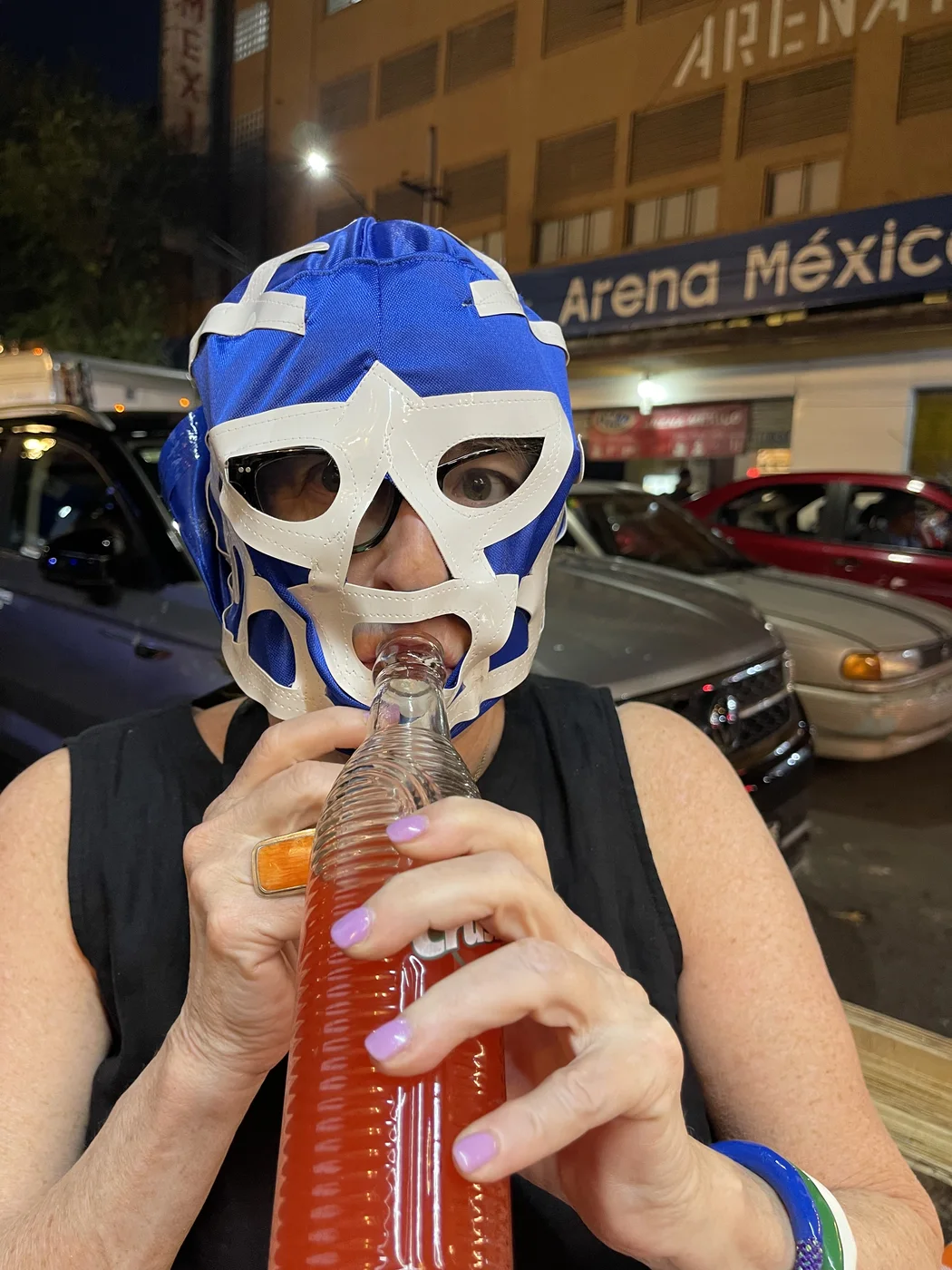 Nancy Hirsch wearing a blue lucha libre mask and drinking a bright red soda